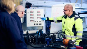 työtakkinen mies esittelee hydraulikkamittaristoa opiskelijiolle