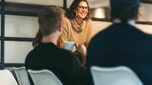 Nainen neuvotteluhuoneessa hymyilee istuville kuulijoille.