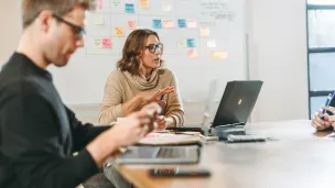 Kolme ihmistä kokouksessa pöydän ääressä, kannettavat ja muistiinpanot.