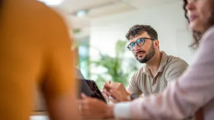 Kolme ihmistä keskustelee toimistossa.