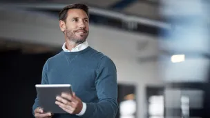 Mies pitelee tablettia ja katsoo sivulle hymyillen sisätiloissa.
