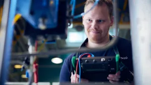 Mies tutkii koneen osia tehtaassa keskittyneesti.