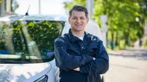 Hymyilevä kiinteistönhoitaja nojaa autoon pihalla