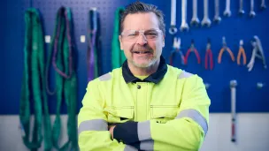 Mies huomiotakissa hymyilee työkaluseinän edessä.