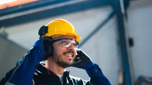 Rakennustyöntekijä kypärä päässä, hymyilee sisätiloissa.