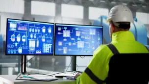 Mies tietokoneen näyttöjen edessä voimalaitoksessa