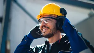 Rakennustyömaan työntekijä käyttää keltaista kypärää ja suojalaseja.