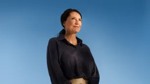 Woman in blue shirt standing against a blue background.