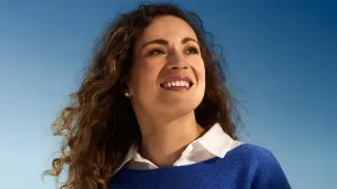 Smiling woman with curly hair against a blue sky background.