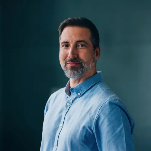 Mies hymyilee vaaleansinisessä paidassa, tumma tausta. Valokuva.