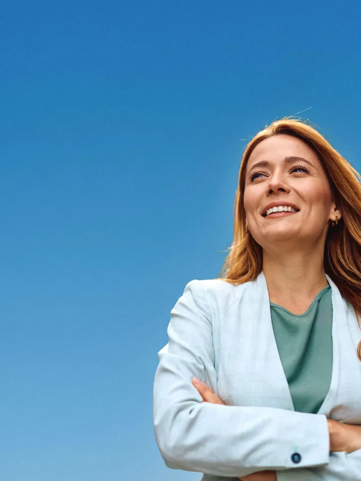 Smiling woman in a light suit stands against a clear blue sky.