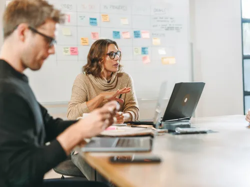 Kolme ihmistä kokouksessa pöydän ääressä, kannettavat ja muistiinpanot.