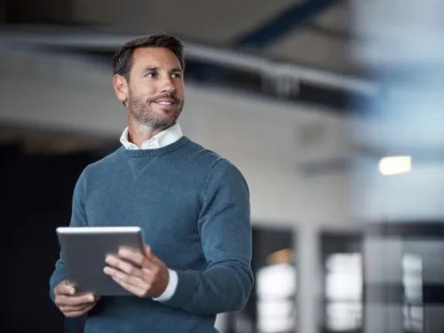 Mies pitelee tablettia ja katsoo sivulle hymyillen sisätiloissa.