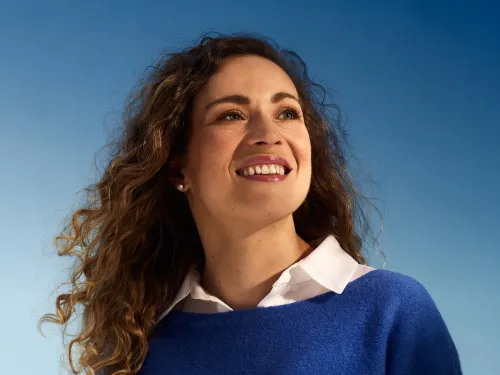 Smiling woman with curly hair against a blue sky background.
