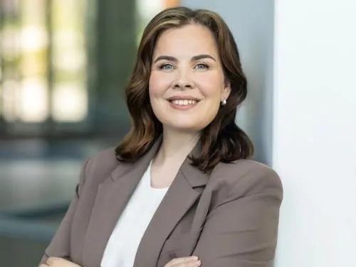 Professional woman smiling, arms crossed, wearing a beige blazer.