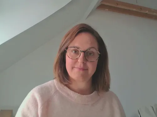 Nainen hymyilee huoneessa, jossa on valkoiset seinät ja viistokatto.